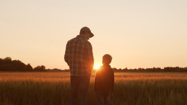 Farmer and his son in front of a sunset agricultural landscape. Man and a boy in a countryside field. The concept of fatherhood, country life, farming and country lifestyle.