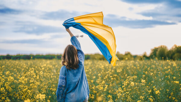 Ukrainian patriot woman waving national flag in canola yellow field. Rare, back view. Ukraine unbreakable, peace, independence, freedom, victory in war.