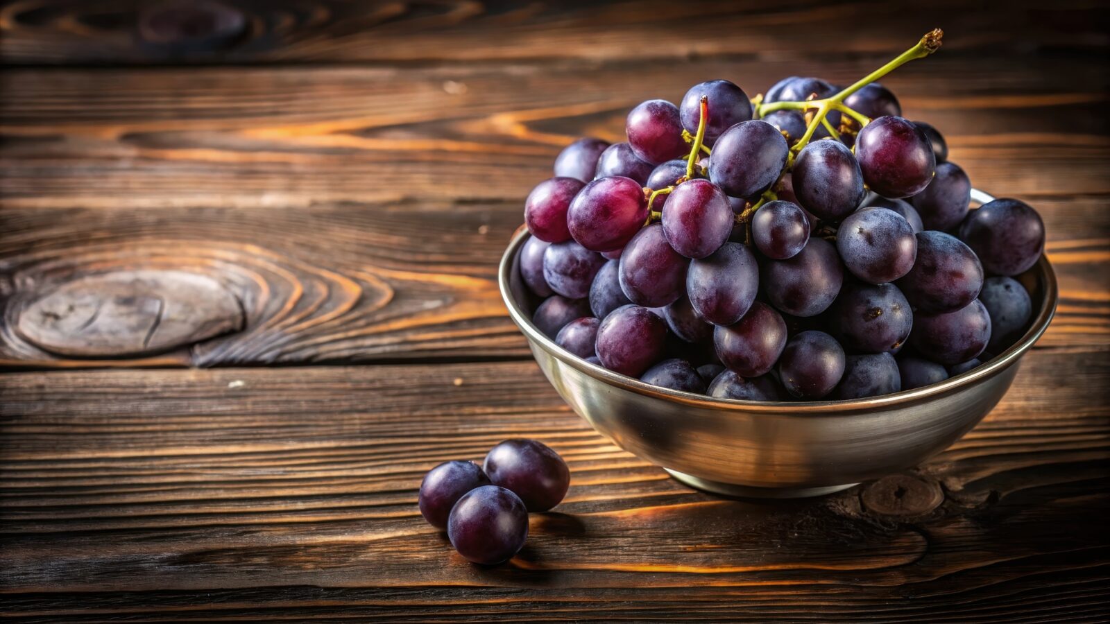 Dark purple grapes in a modern metallic bowl on a wooden surface
