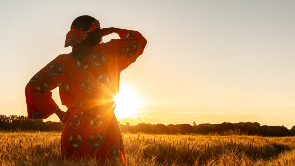 African woman in traditional clothes standing in a field of crops at sunset or sunrise