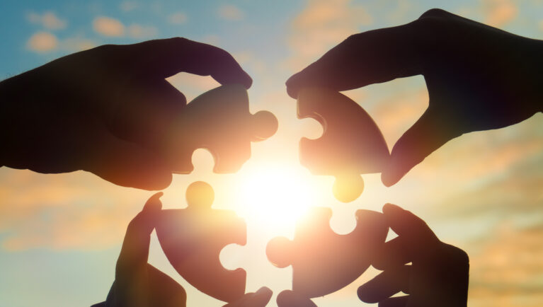 Four hands of businessmen put together a puzzle against the backdrop of a dramatic sky at sunset. Business concept idea, collaboration, teamwork, partnership, innovation