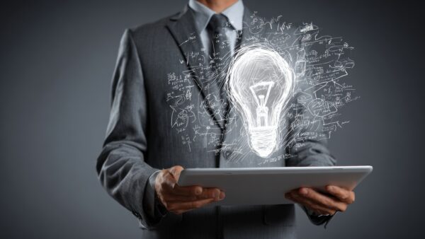 A businessman in a suit holds a digital tablet, from which a bright, glowing lightbulb emerges, symbolizing ideas and innovation.