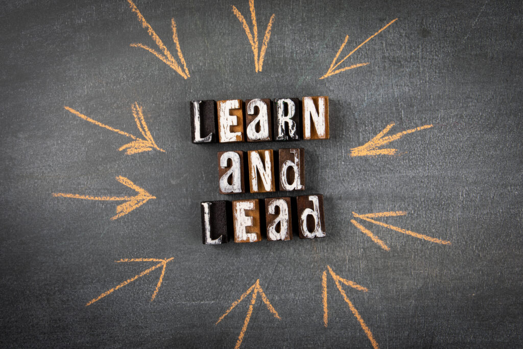 Learn and Lead. Letters of the alphabet with text on a dark chalk board