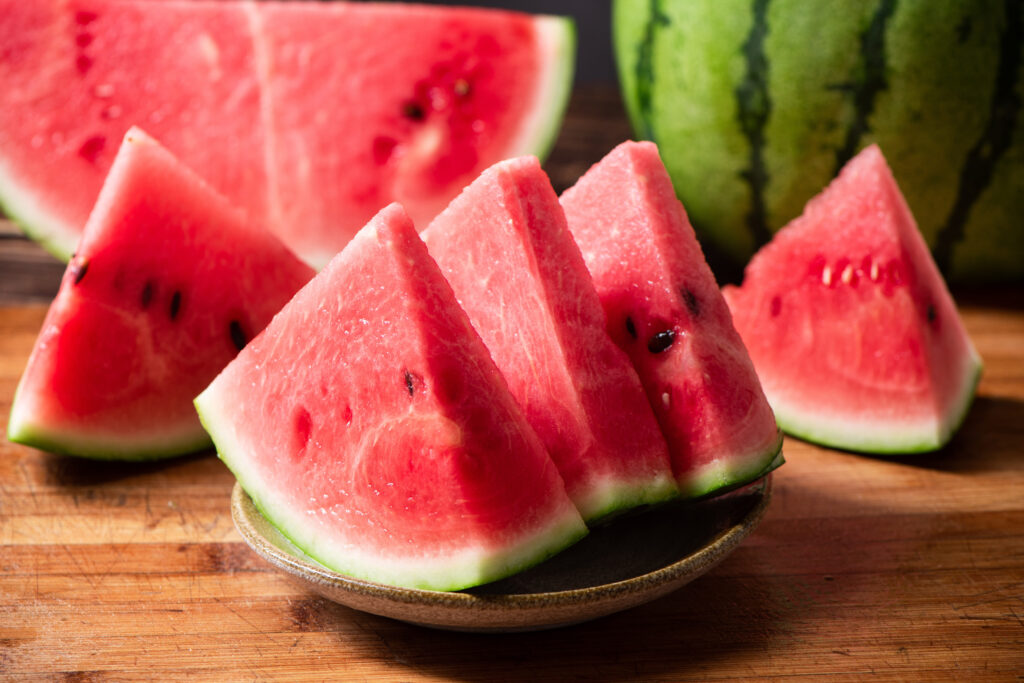 Sliced watermelon on bamboo board over white wooden surface, side view. Close-up.