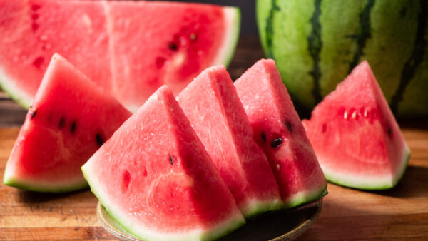 Sliced watermelon on bamboo board over white wooden surface, side view. Close-up.