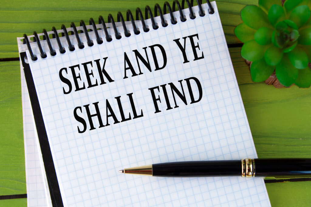 SEEK AND YE SHALL FIND - words in a white notebook on a green wooden background with a cactus and a pen