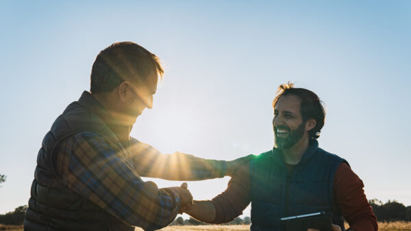 Two happy farmers shaking hands in a cultivated field at sunset, making a business agreement