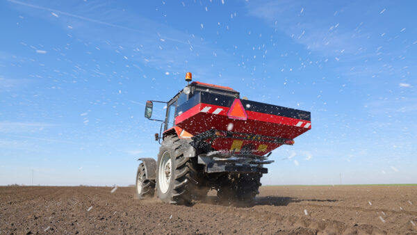 Spreading mineral fertilizer, low angle shot. Farmer with agricultural machinery fertilizing agricultural field in spring time.