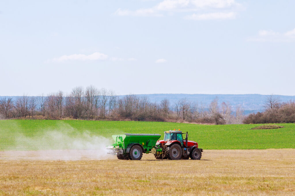Tractor spreading fertilizer on grass field. Agricultural work.