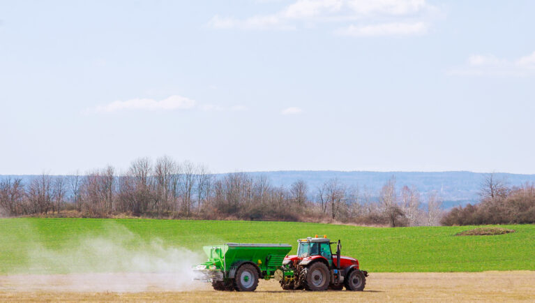 Tractor spreading fertilizer on grass field. Agricultural work.