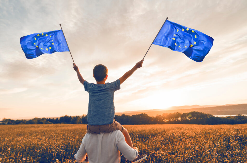 Patriotic father and child waving European Union flag on sunset
