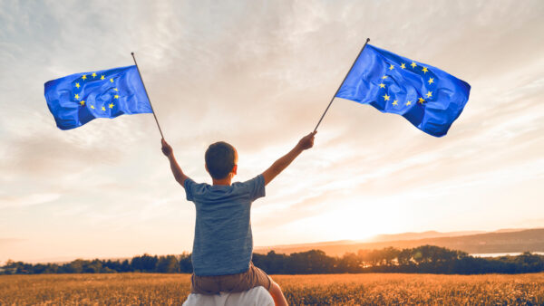 Patriotic father and child waving European Union flag on sunset