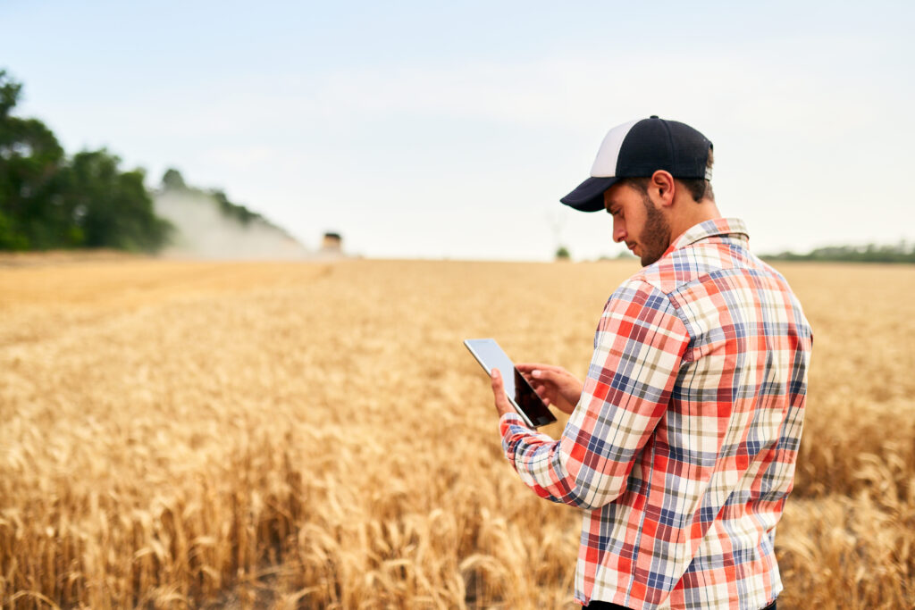 Smart farming using modern technologies in agriculture. Man agronomist farmer holding digital tablet computer standing in a wheat field and using apps, internet for business management and analytics
