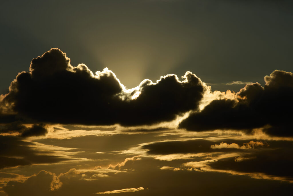 massive dark clouds dramatically backlit by intense golden sunlight breaking through the cloud cover. Spectacular crepuscular rays radiate Super El Niño climate phenomenon and global warming