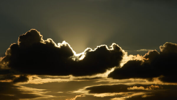 massive dark clouds dramatically backlit by intense golden sunlight breaking through the cloud cover. Spectacular crepuscular rays radiate Super El Niño climate phenomenon and global warming